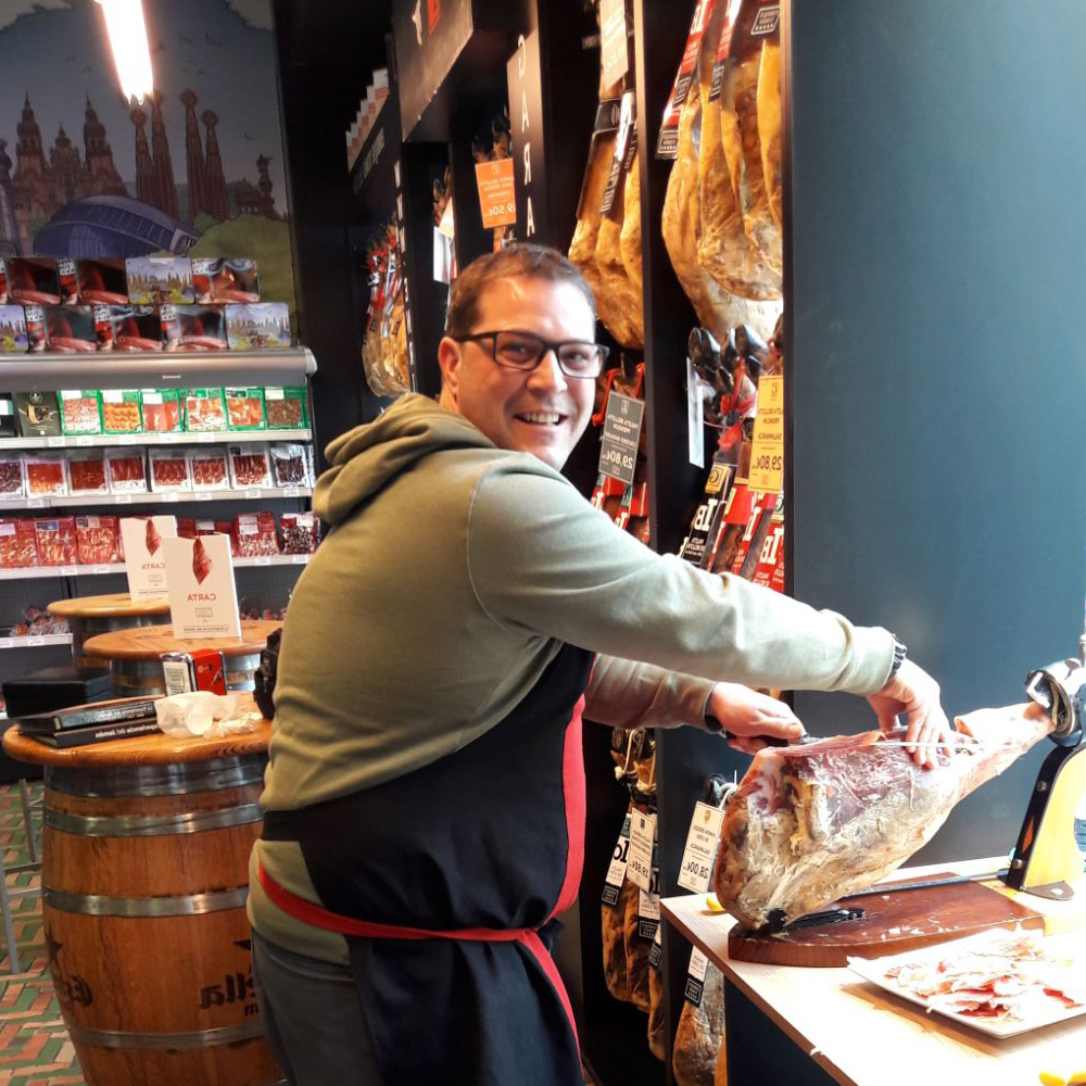 Raoul, chef de Mister Tapas Paella, tranchant un jambon ibérique dans sa boutique spécialisée en produits espagnols